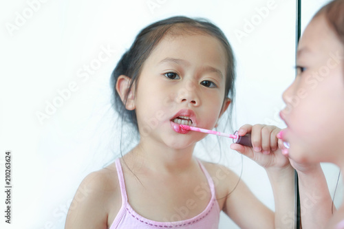 Cute little Asian child girl trying lip gloss near a mirror. 