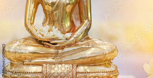 Closeup golden Buddha statue with Jasmine flower on hands.
