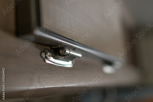 A tiny silver hinge connecting a wooden panel to a cabinet face making a small door.