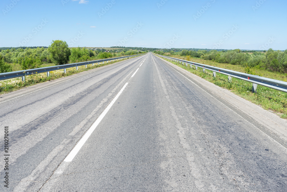 Obraz premium Vanishing straight highway with metal rails along. Kozelsk, Kaluzhsky region, Russia.