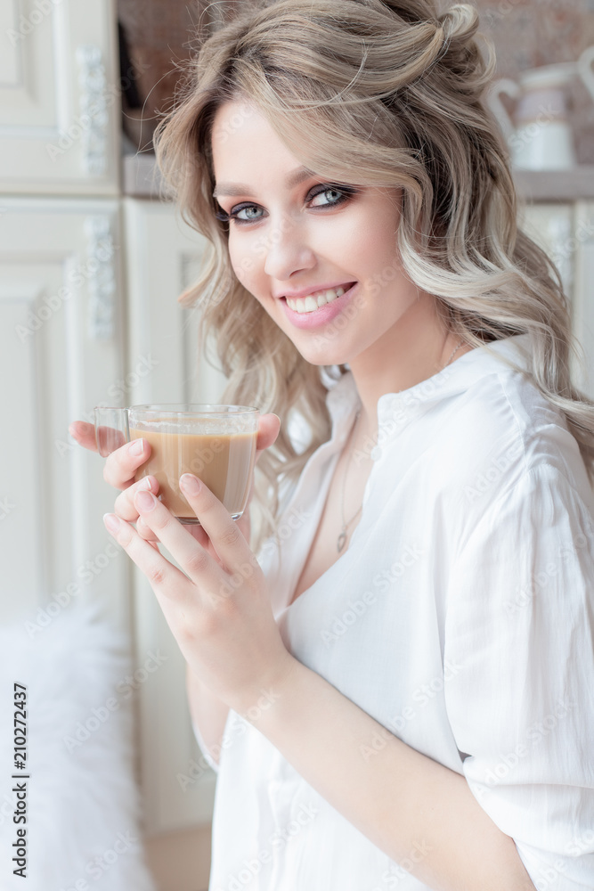 beautiful cute girl near the window in the morning in a white shirt with a cup of coffee beautiful cute girl near the window in the morning in a white shirt with a cup of coffee