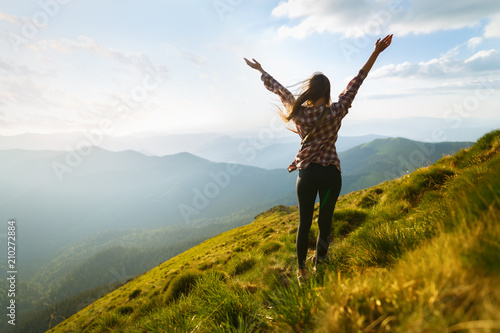 Hiker woman standing with hands up achieving the top. Girl welcomes a sun. Conceptual design. Successful woman hiker open arms on sunrise mountain top. Happy young blonde woman portrait