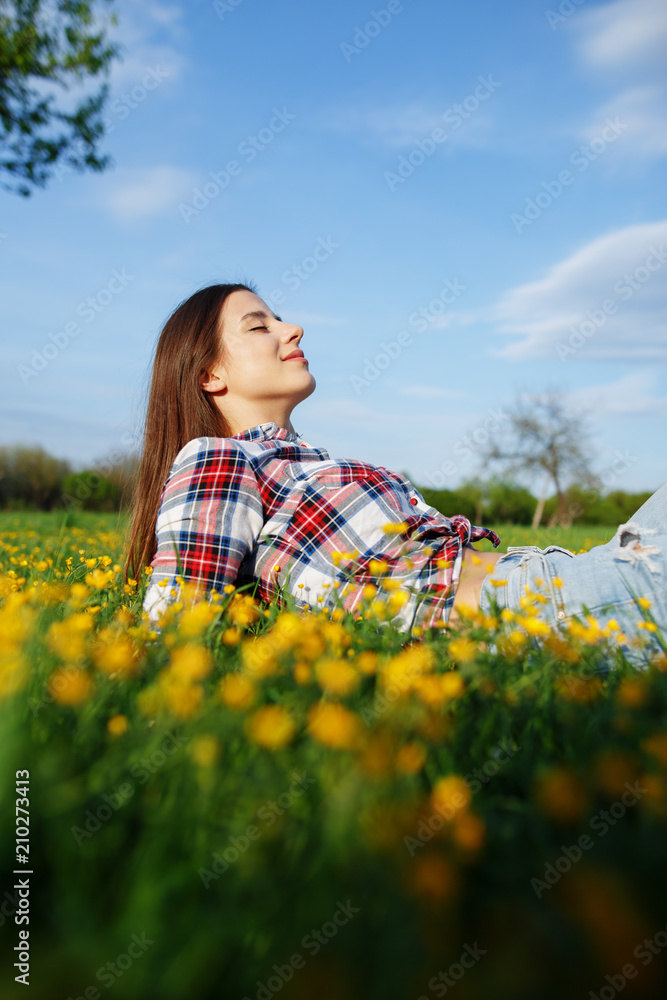 Beautiful smiling woman in plaid shirt and jeans lying on a grass outdoor. Beautiful woman lying down in the meadow of flowers. Pretty girl relaxing outdoors on spring grass Beautiful smiling woman in plaid shirt and jeans lying on a grass outdoor. Beautiful woman lying down in the meadow of flowers. Pretty girl relaxing outdoors on spring grass