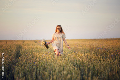 girl with flowers walking on a grain field.