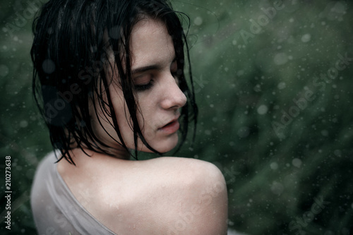 Wet hair woman portrait in wet clothes sitting on the grass under the summer rain