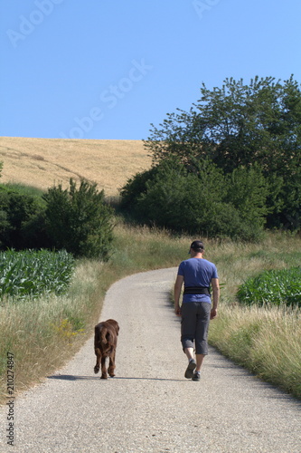 A man is walking with a dog flat coated retriever on a rural road © Elvira