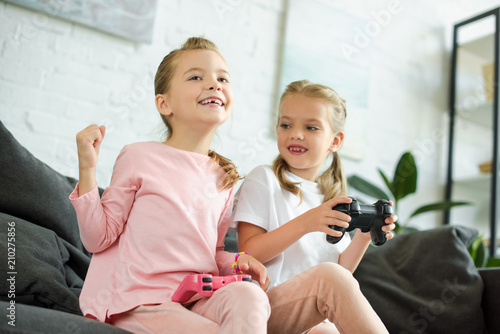 portrait of little sisters with gamepads playing video game together at home