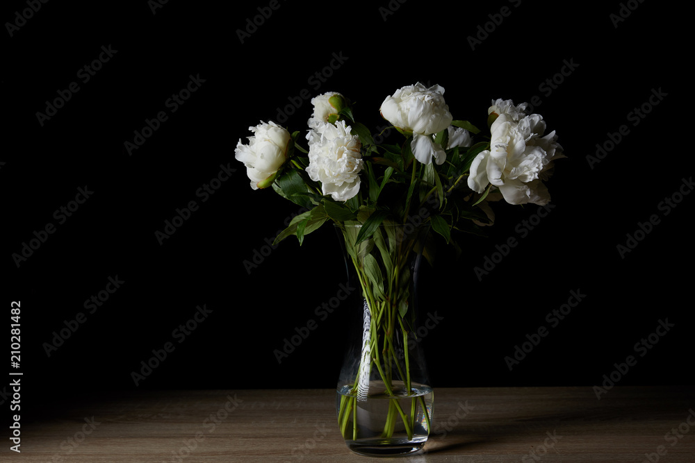 beautiful white peonies in glass vase on wooden table and on black