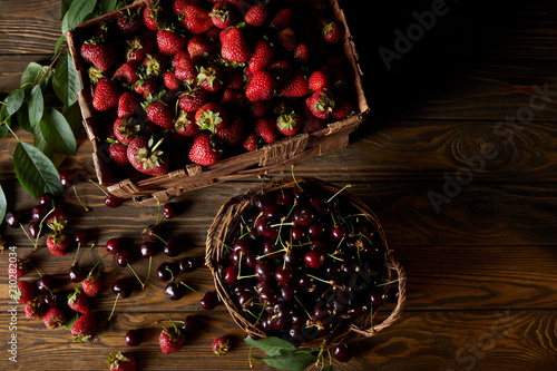 top view of cherries and strawberries in basket and box on wooden tabletop