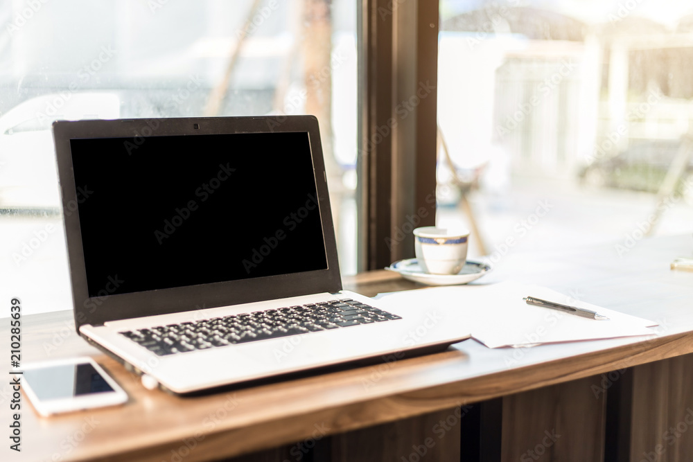 Mockup image of laptop with blank black screen,smartphone,coffee cup on wooden table of In the coffee shop. Mockup image of laptop with blank black screen,smartphone,coffee cup on wooden table of In the coffee shop.