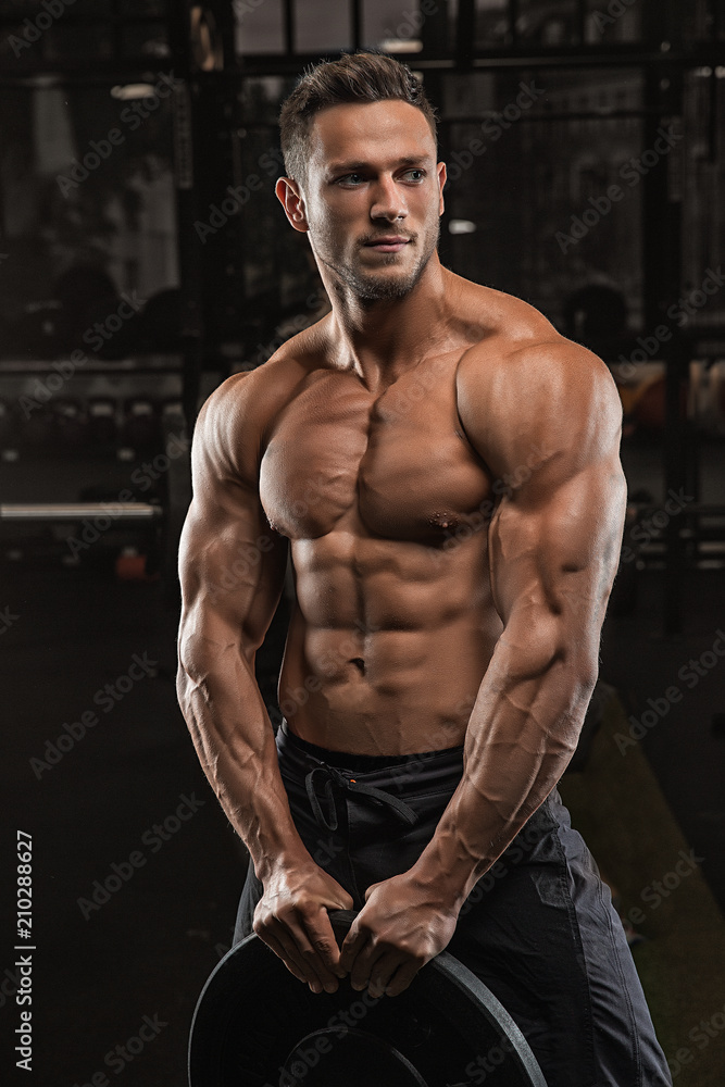 Young handsome sportsman bodybuilder weightlifter with an ideal body, after coaching poses in front of the camera, abdominal muscles, biceps triceps. In sportswear.