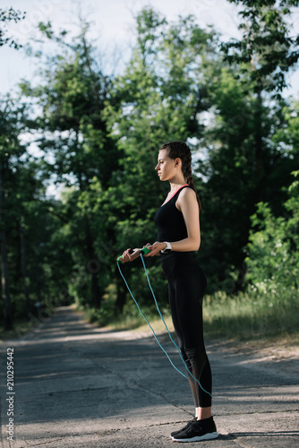 sportswoman exercising with jump rope on path in park