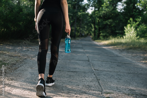 cropped view of sportswoman with sports bottle of water walking on path