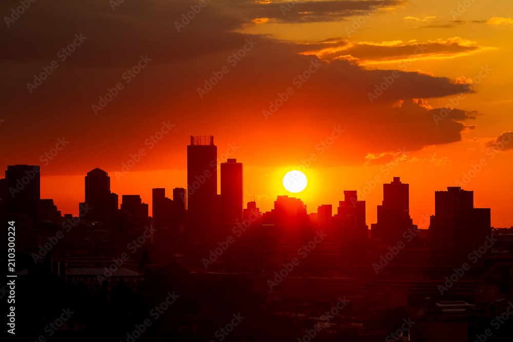 Dramatic cloudy sky at sunset in urban area. Silhouette buildings and lens flare from the sun
