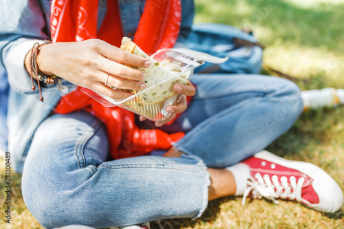 Young woman eating sandwich and having lunch break outdoors in park