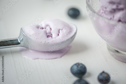 Melted blueberry ice cream in a spoon on white wooden table with berries. Shallow depth of field. Close-up..