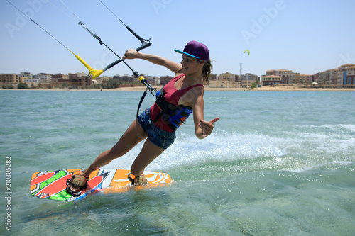Kite surfing girl in sexy swimsuit with kite in sky on board in blue sea riding waves with water splash. Recreational activity, water sports, action, hobby and fun in summer time. Kiteboarding sport