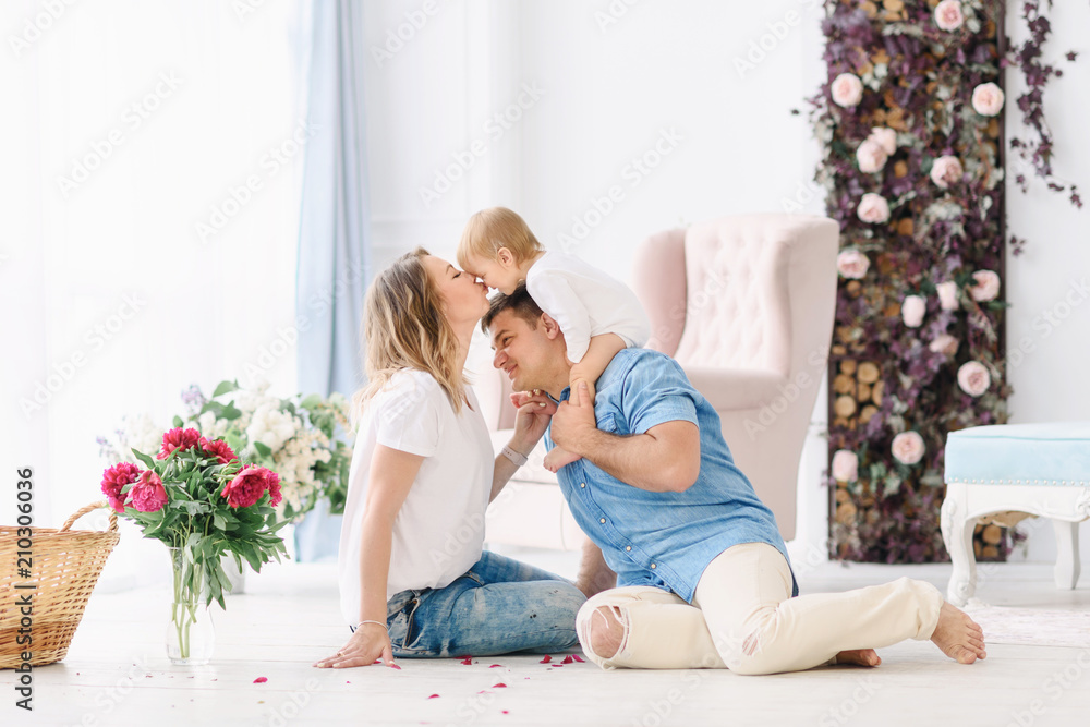 Young parents play with their young child in a spacious bright room. Mom and Dad hug and kiss each other Young parents play with their young child in a spacious bright room. Mom and Dad hug and kiss each other