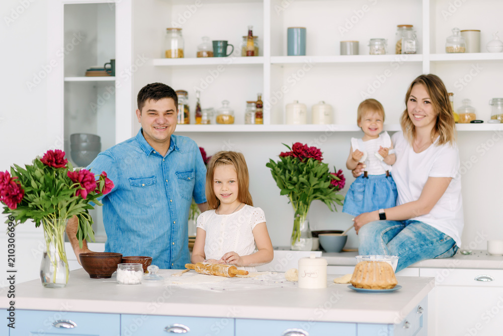 Young parents prepare a delicious and healthy breakfast in a large bright kitchen with their two lovely children. Dad kisses and hugs mother, children are happy Young parents prepare a delicious and healthy breakfast in a large bright kitchen with their two lovely children. Dad kisses and hugs mother, children are happy