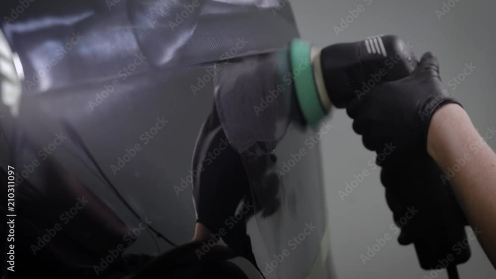 man is spreading gloss over surface of black auto with rotating electric polishing machine, close-up man is spreading gloss over surface of black auto with rotating electric polishing machine, close-up