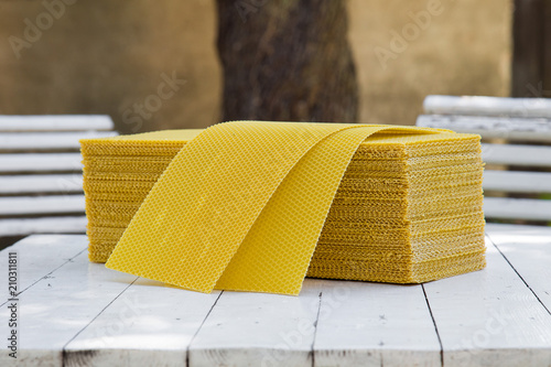 Plates of wax foundation - stack of apiary honeycomb base elements on wooden table.