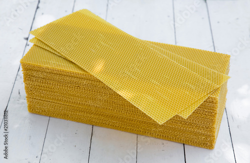 Plates of wax foundation - stack of apiary honeycomb base elements on wooden table.