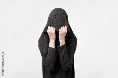 Woman hiding face under the clothes. She is oulling sweatr on her head. Depressed emotion. photo