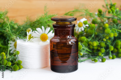 Pharmacy bottle with cosmetic/cleansing/healing wild chamomile aroma oil or tincture and cotton pads for natural skin care and medicinal purposes. Homemade cosmetics and phytotherapy.  photo