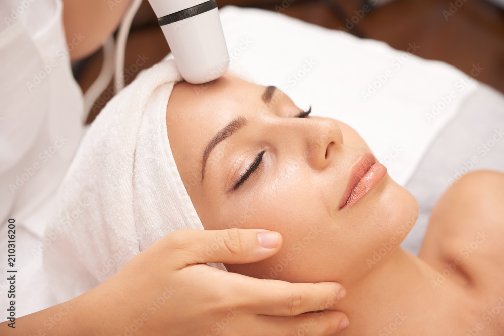 Relaxed woman enjoying facial beauty procedure carried out with special electric device