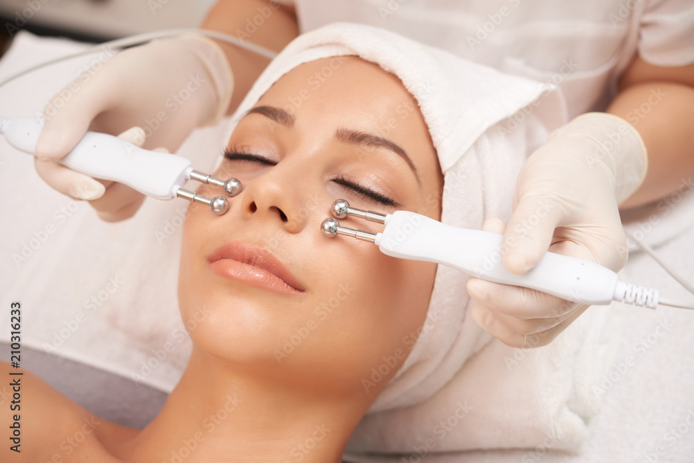 Young client of cosmetic salon having relaxing procedure on her face with special devices Young client of cosmetic salon having relaxing procedure on her face with special devices