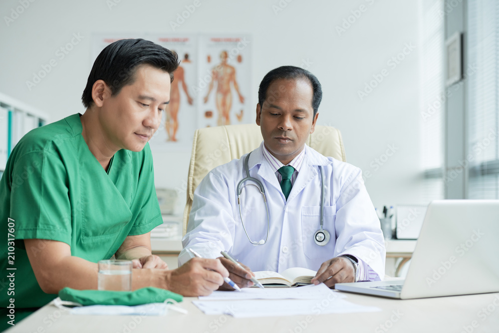 Two doctors sitting at the table and working in team at office Two doctors sitting at the table and working in team at office