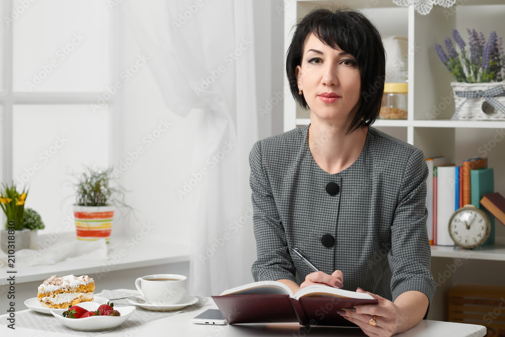 the business woman reading the diary, dressed in a gray suit poses in front of a white wall the business woman reading the diary, dressed in a gray suit poses in front of a white wall