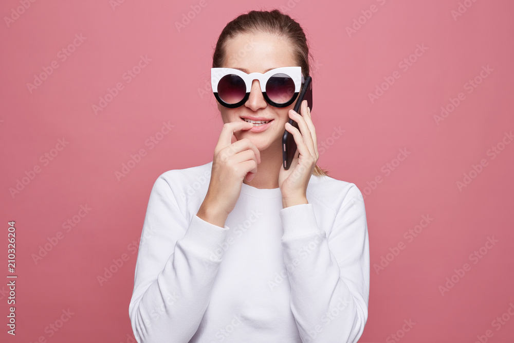 Worried seductive female model bites finger with tender smile, holds modern smart phone in black case, feels frustrated as has failure of payment. Pretty lady ask husband to buy new pair of shoes. Worried seductive female model bites finger with tender smile, holds modern smart phone in black case, feels frustrated as has failure of payment. Pretty lady ask husband to buy new pair of shoes.