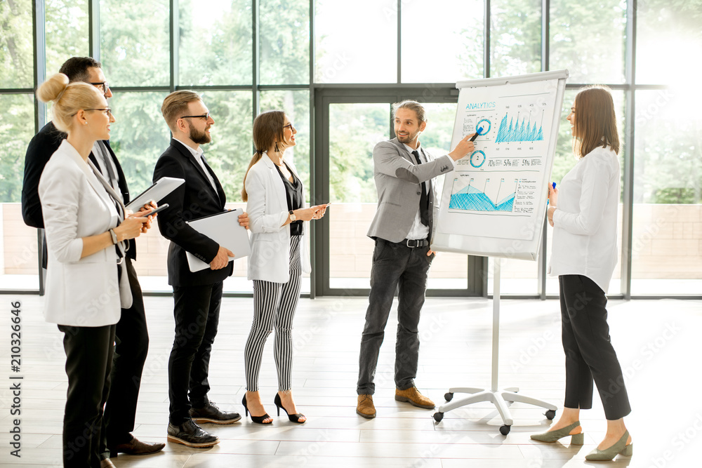A group of business people standing together during the conference with flip chart at the modern office A group of business people standing together during the conference with flip chart at the modern office