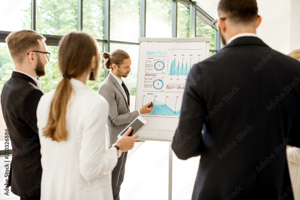 Handsome speaker with flip chart reporting during the conference with business people at the modern office