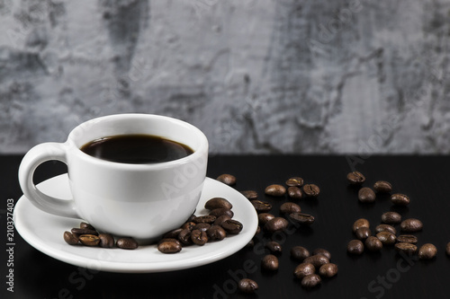 Still life with white cup with delicious coffee and coffee beans on dark background