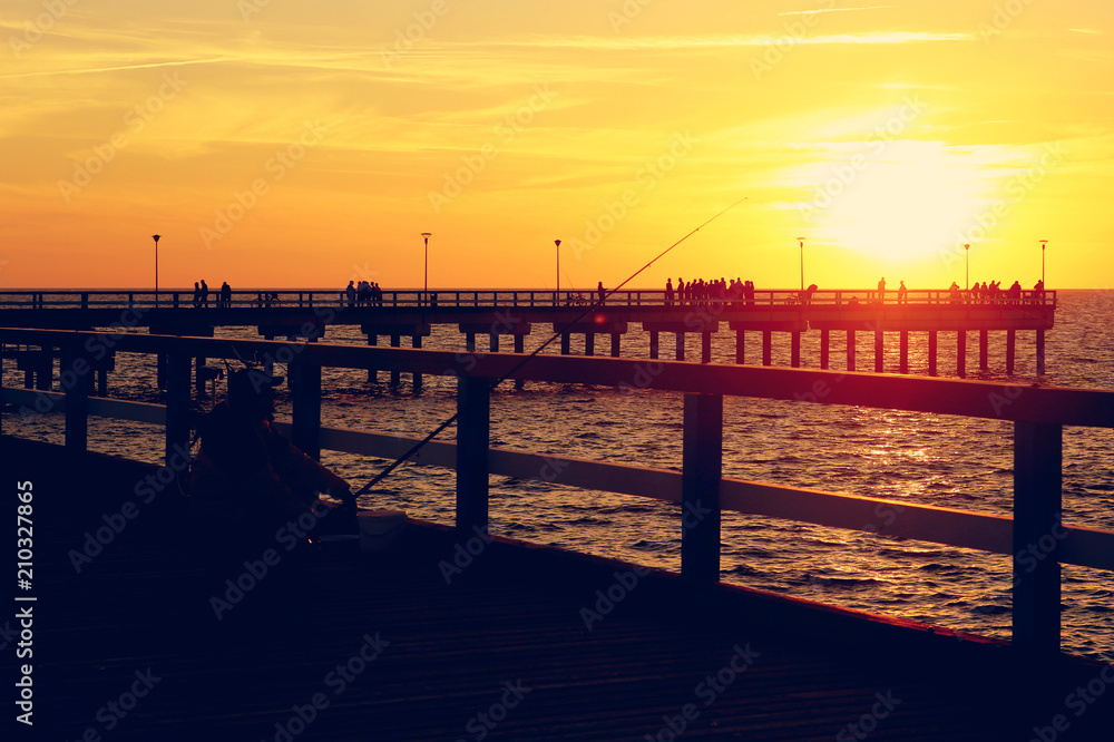 Silhouette of sea bridge with people and fisherman at sunset. Baltic sea beach bridge in Palanga, Toned.