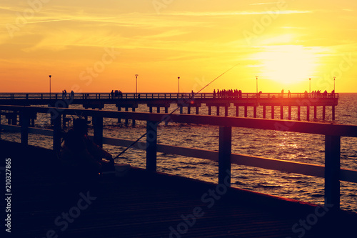 Silhouette of sea bridge with people and fisherman at sunset. Baltic sea beach bridge in Palanga  Toned.