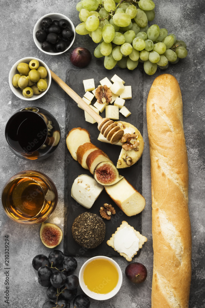Snacks with wine - various types of cheeses, figs, nuts, honey, grapes, bread on a gray background. Top view. Food background