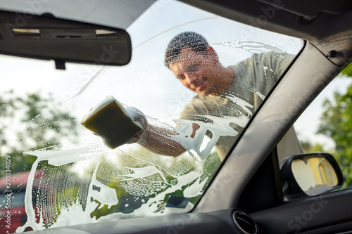 Man is cleaning windows of a car with a sponge and foam.