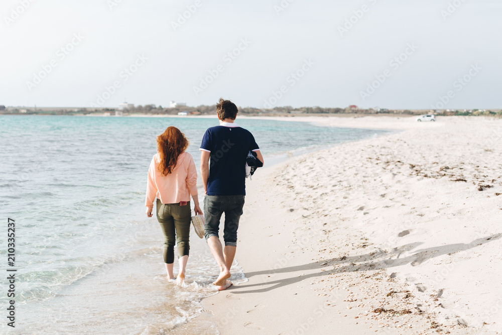 A young couple walking barefoot on the sand on an empty beach.