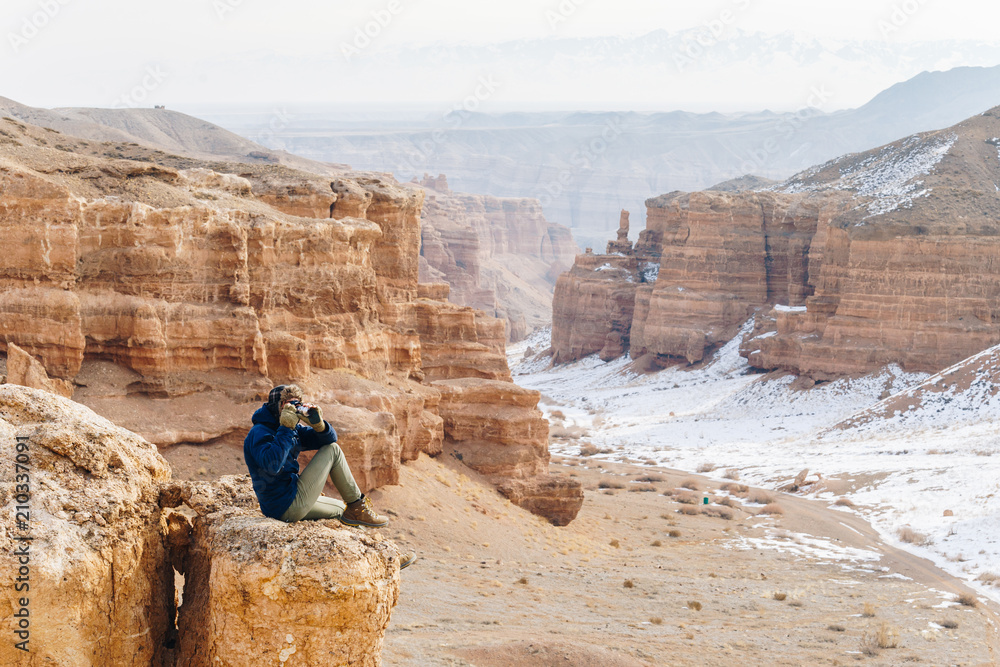 A cheerful traveler with a camera sits on the edge of a cliff in the Charyn canyon in Kazakhstan. Analogue of the American Grand Canyon