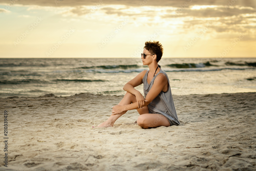 beautiful woman in a gray dress sitting on the beach at sunset