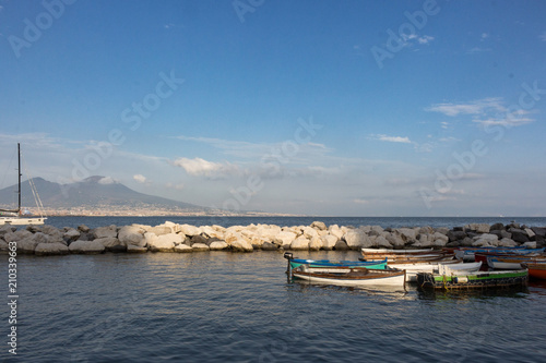 Sailboats in dock against Vesuvius volcano and Mediterranean sea. Boats in harbour in Naples (Napoli), Italy. Sailing and travel concept. Calm evening on seashore. Neapolinan landmark. 