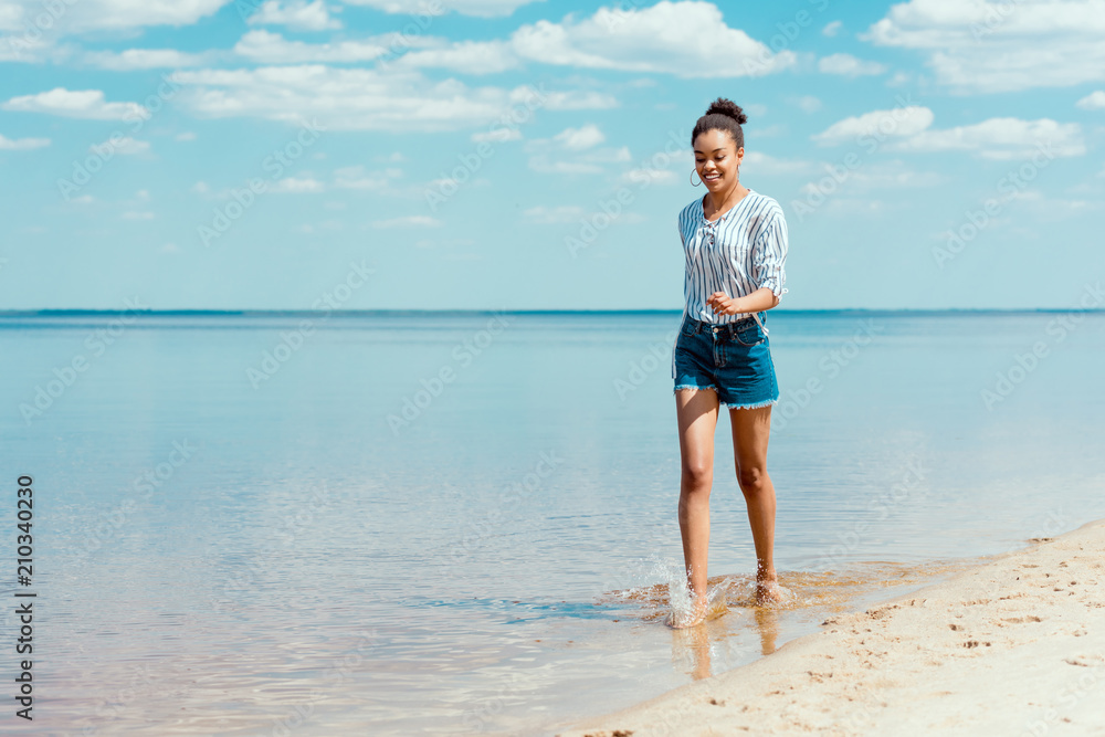 young smiling african american woman walking in sea water near sandy beach young smiling african american woman walking in sea water near sandy beach