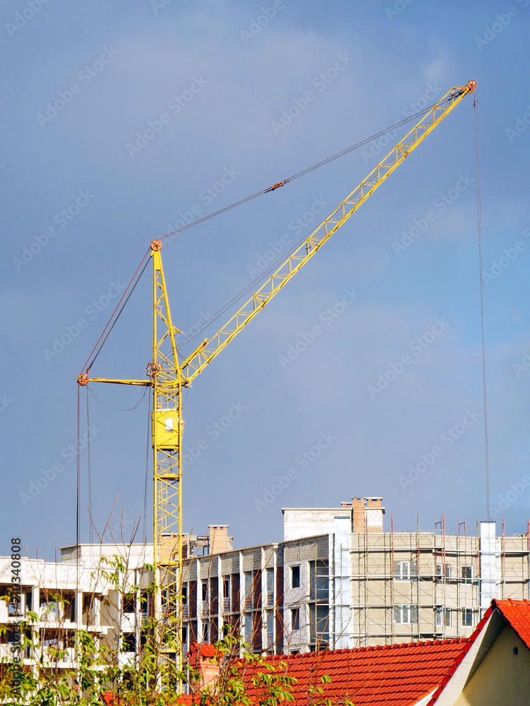 Construction crane near building under construction against blue sky. Construction site.