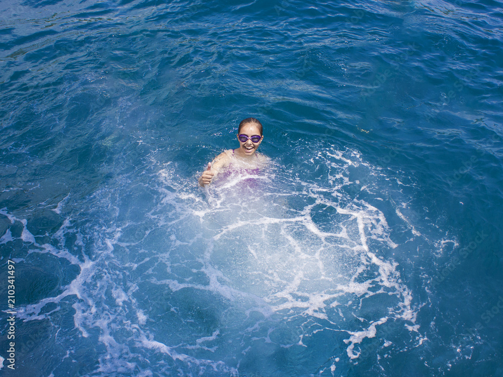 Happy beautiful girl in a sweemsuit and water-glasses splashing in the sea
