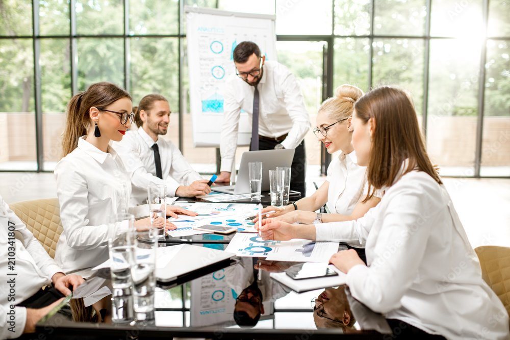 A group of business people strictly dressed in white sitting together during a conference in the spacious office with flip chart on the green background A group of business people strictly dressed in white sitting together during a conference in the spacious office with flip chart on the green background