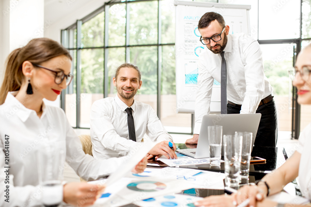 A group of business people strictly dressed in white sitting together during a conference in the spacious office with flip chart on the green background