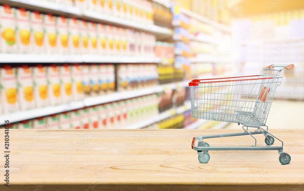 Supermarket with product shelves blur background with empty shopping cart on wood table Supermarket with product shelves blur background with empty shopping cart on wood table